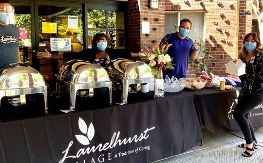Masked employees from Avamere at Laurelhurst preparing a delicious looking buffet outside the front entrance
