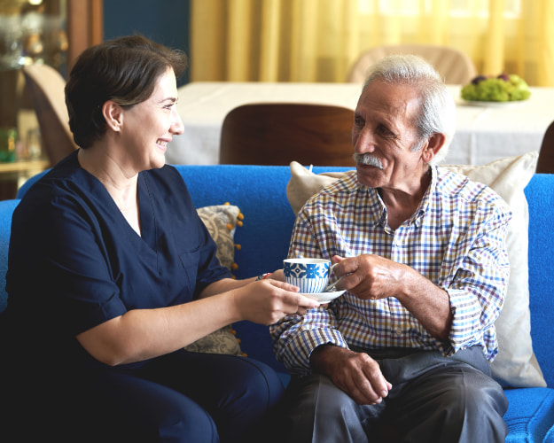 Caregiver passing a cup of tea on a saucer to an elderly gentleman