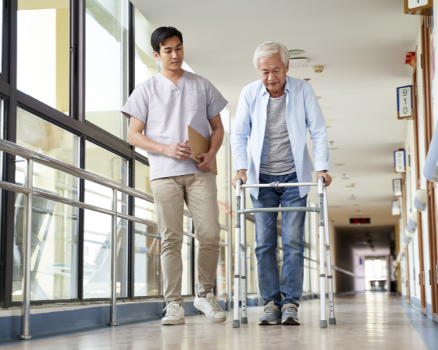 Caregiver walking next to an elderly man using a walker